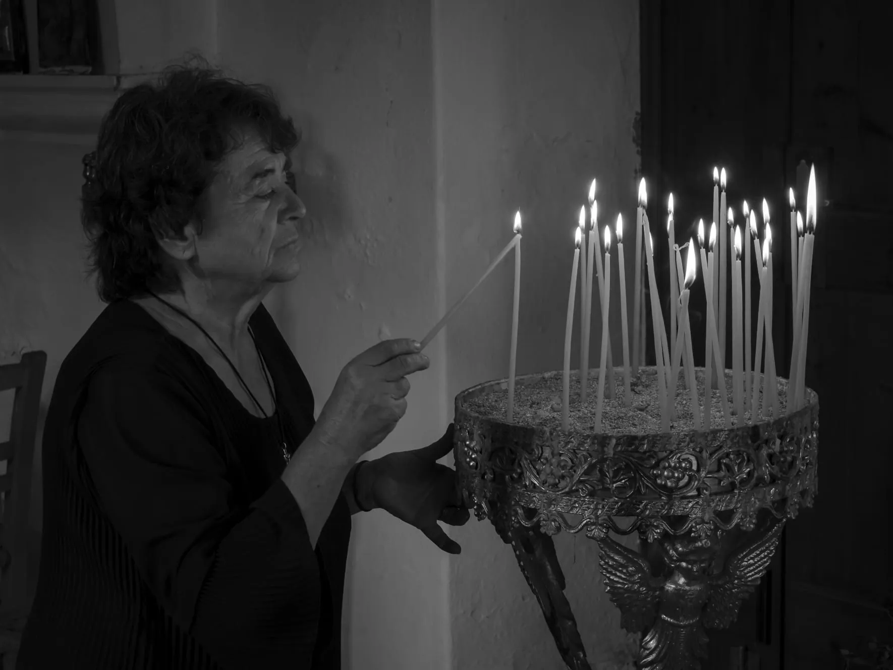 Schwarzweiß: Frau entzündet Kerzen an einem verzierten Kerzenständer in einer Kirche