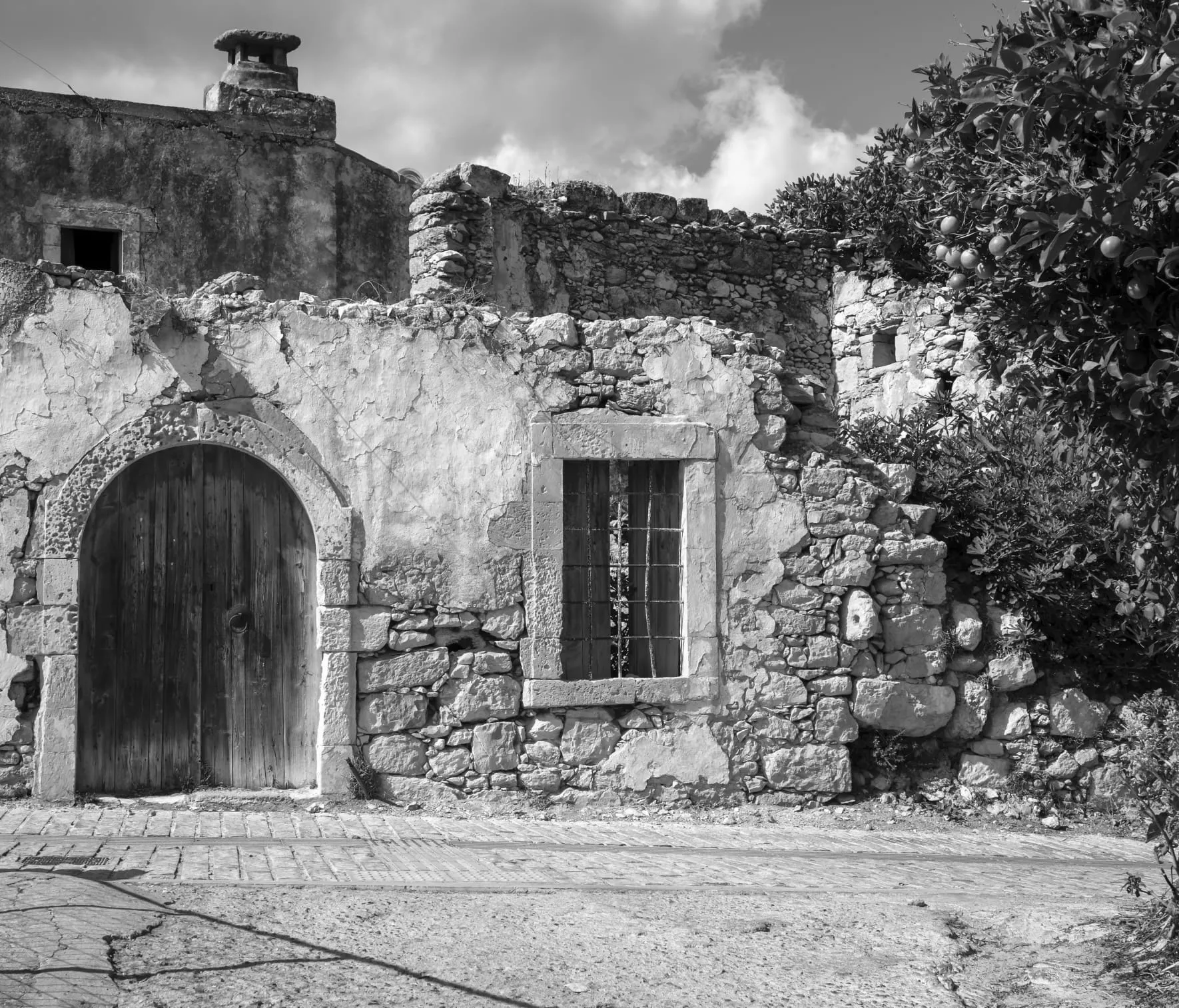 Schwarzweiß: altes Steinhaus mit rundbogigem Holztor und vergittertem Fenster
