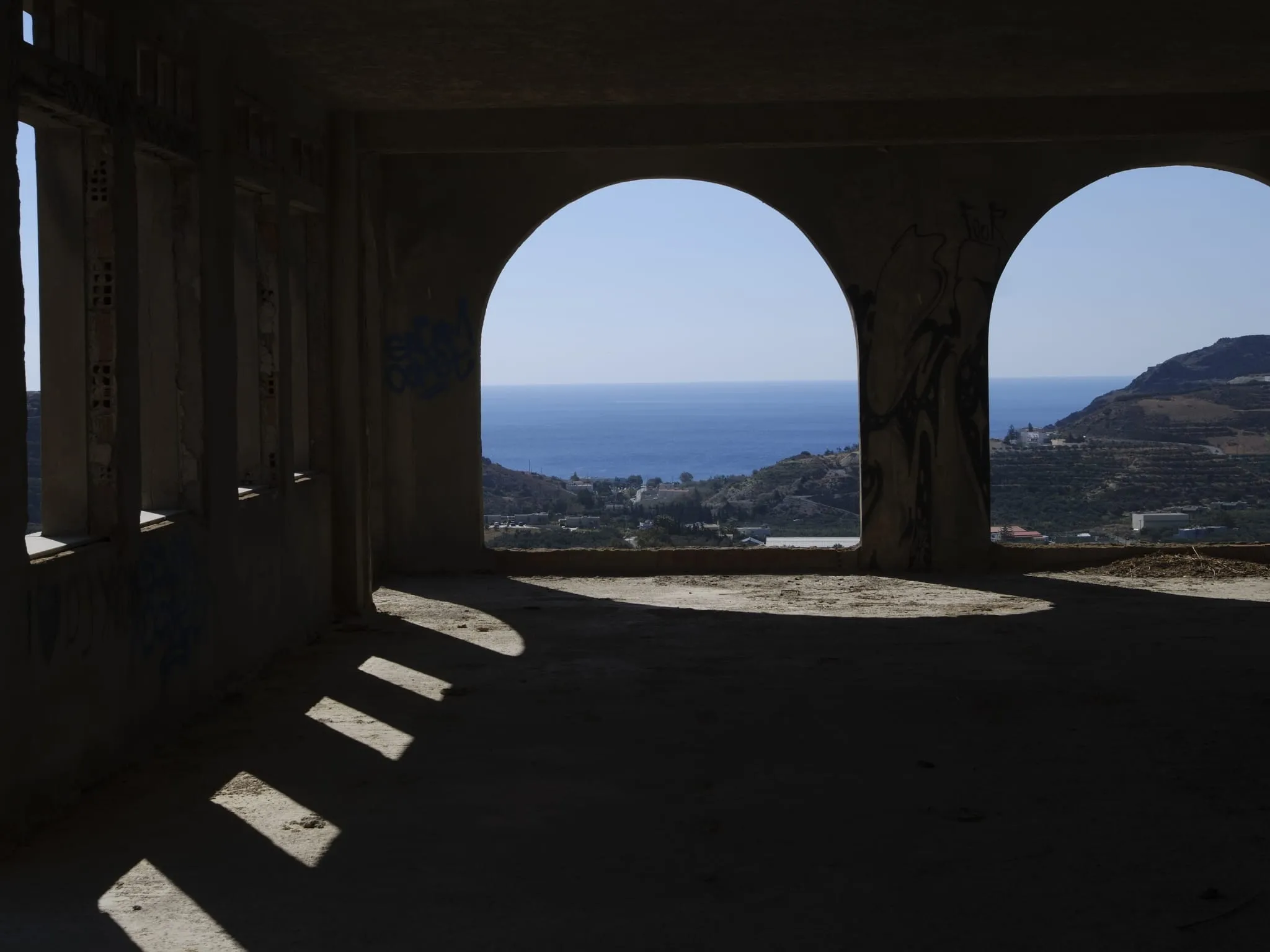Blick durch die Bögen eines unfertigen Betonbaus auf das Meer