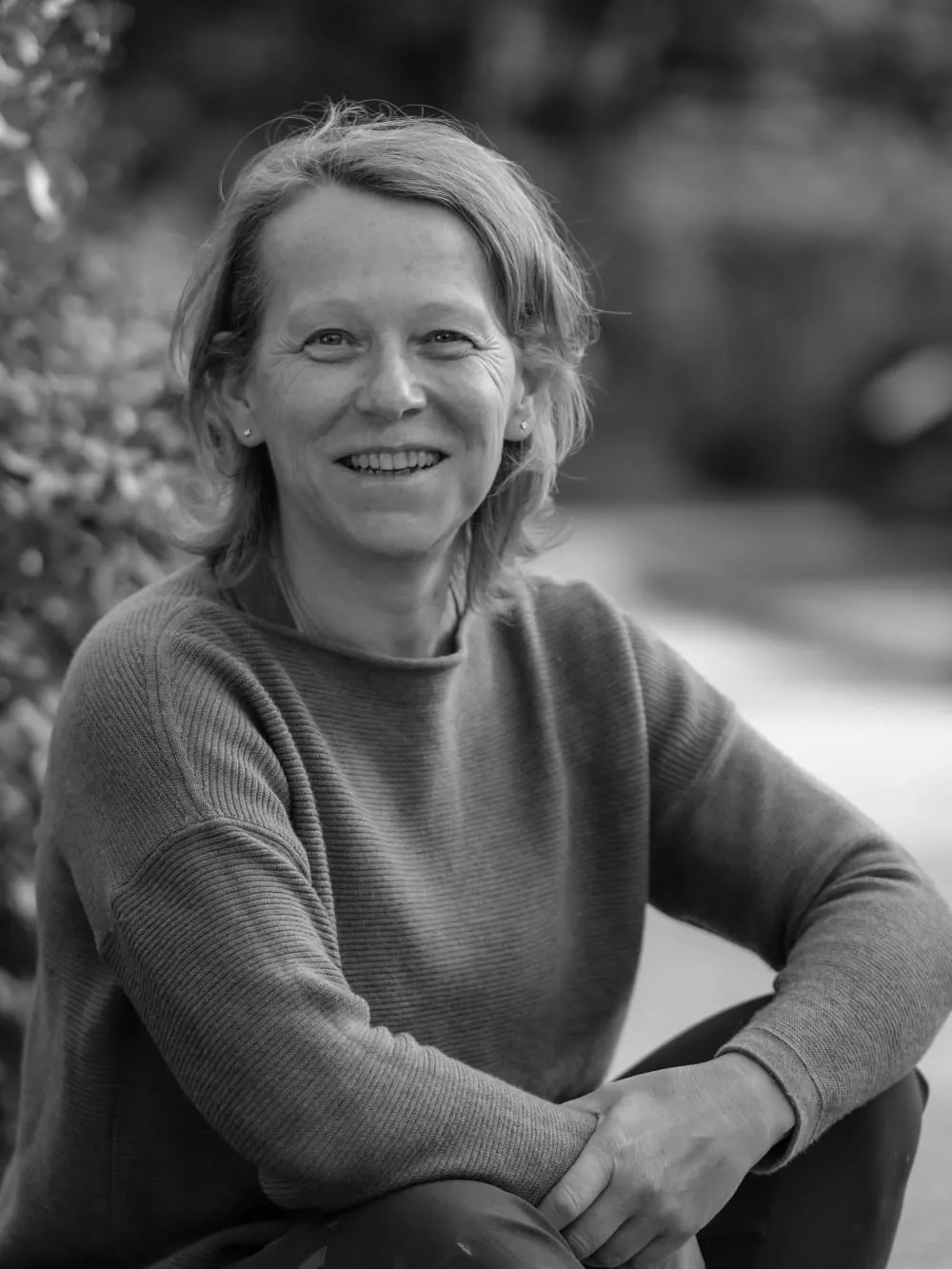 Schwarzweiß-Portrait einer lachenden Frau im Strickpullover, im Freien sitzend