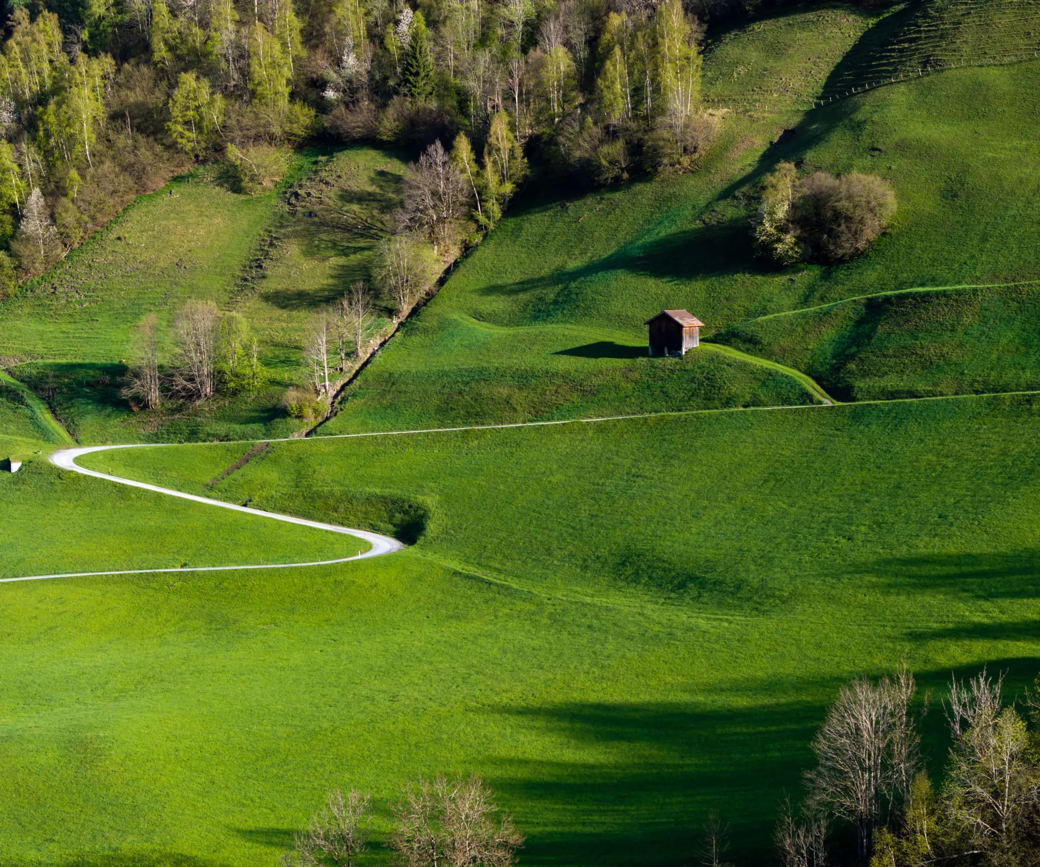 Sattgrüne Wiesenhänge mit einem geschwungenen Weg und einer kleinen Holzhütte
