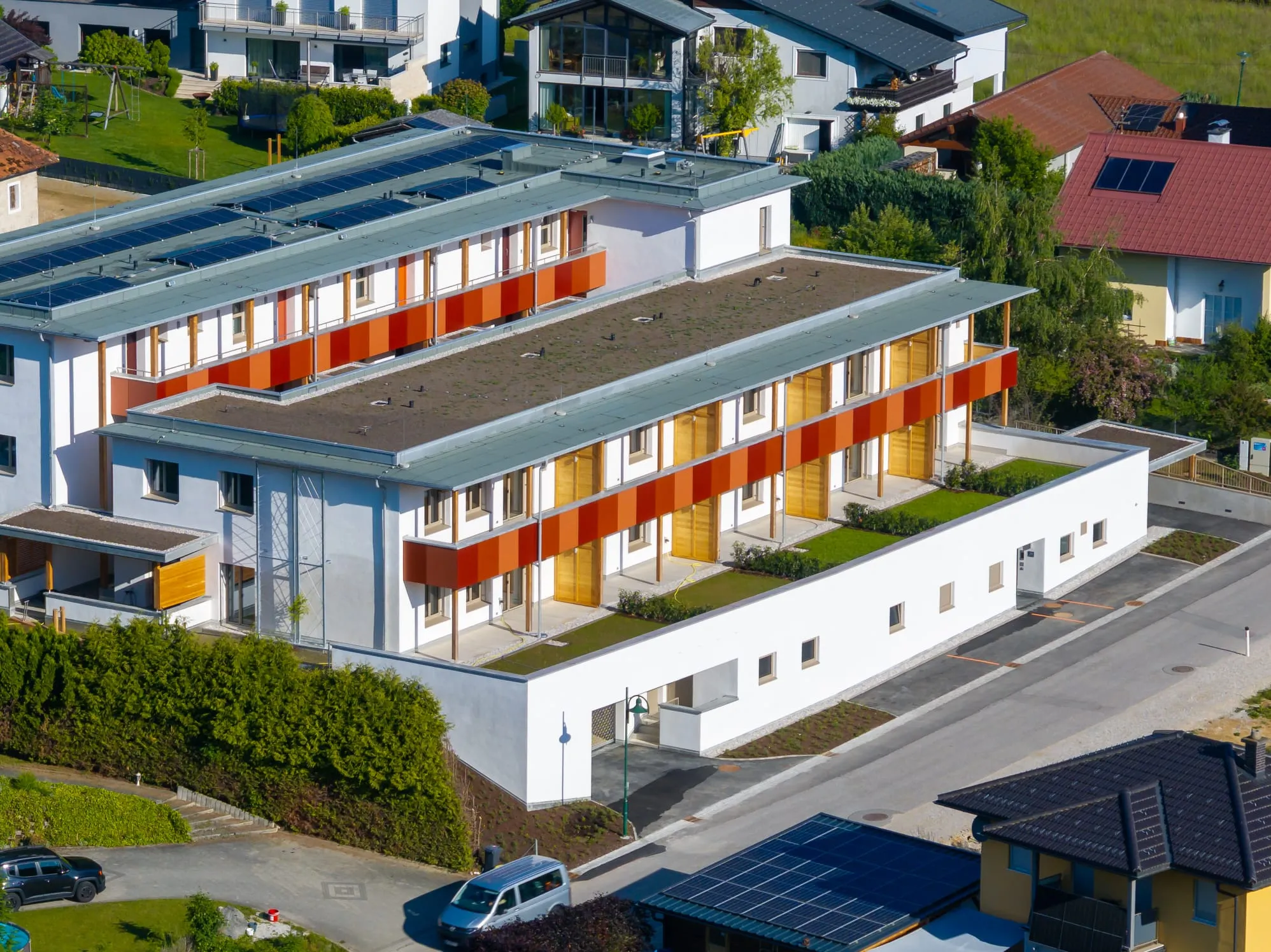 Schräge Luftaufnahme einer modernen Wohnanlage mit begrüntem Flachdach und orange-gelben Fassadenpaneelen
