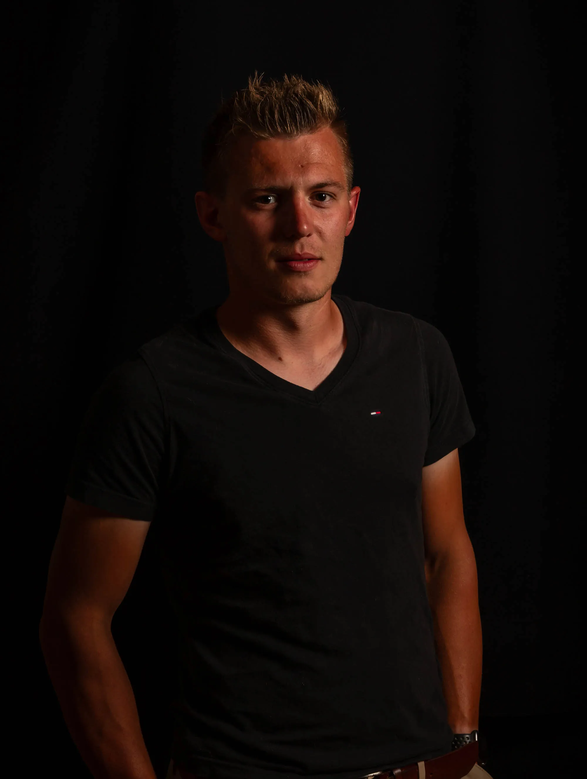 Junger Mann mit blondem Haar im schwarzen T-Shirt vor dunklem Studiohintergrund